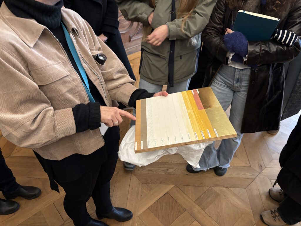 Eine Restauratorin erklärt anhand einer Tafel die Malschichten bei der Vergoldung von Gemälderahmen.